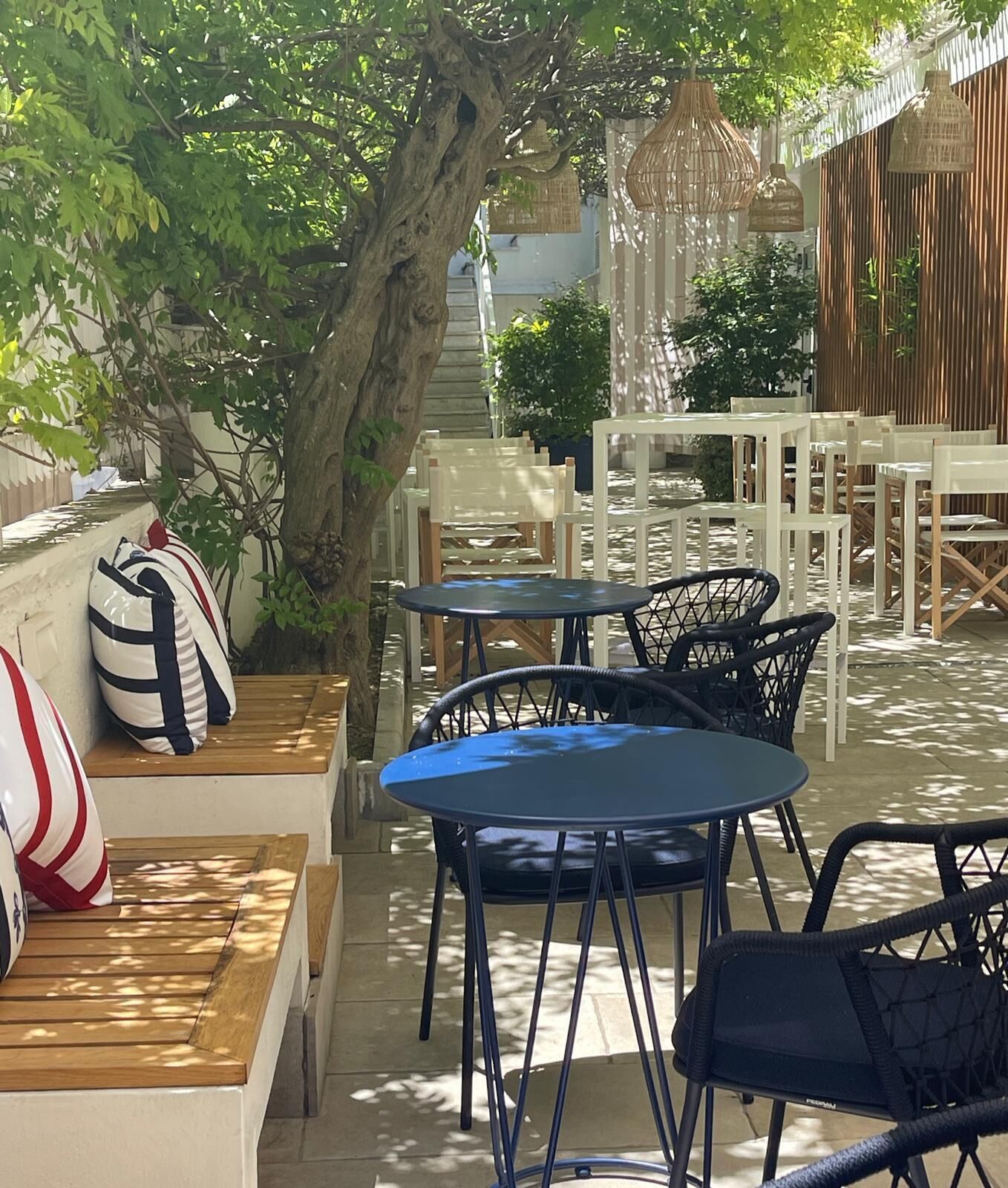 An outdoor seating area with round tables and chairs, a tree, and a bamboo fence.
