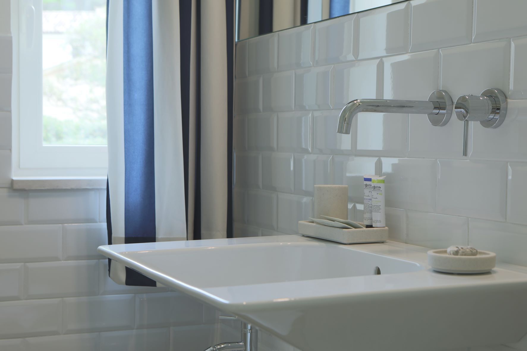 Une salle de bain moderne avec un lavabo blanc, un miroir et une fenêtre ornée de rideaux bleus.