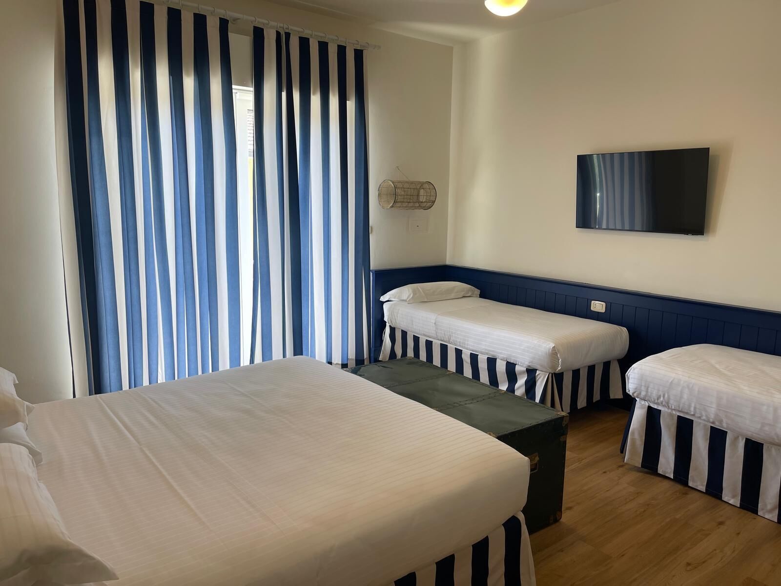 A hotel room with two single beds, a large flat-screen TV, and a window with blue and white striped curtains.