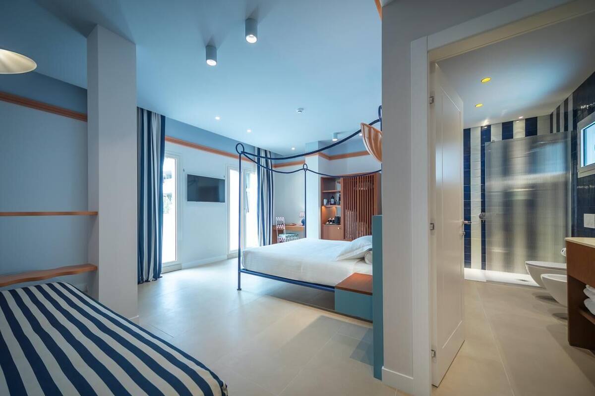 A modern bedroom with a bed, a desk, and a bathroom visible through an open door.
