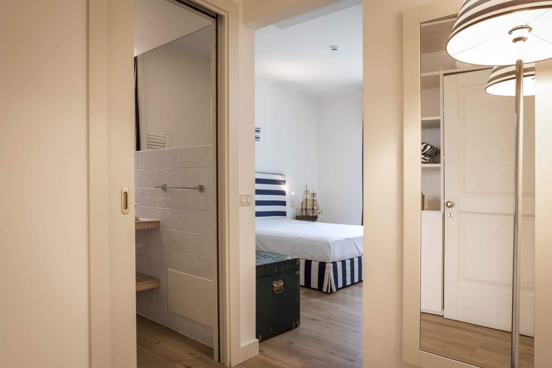A bedroom with a bed, a nightstand, and a dresser. There is a door leading to a bathroom with a shower and a toilet.