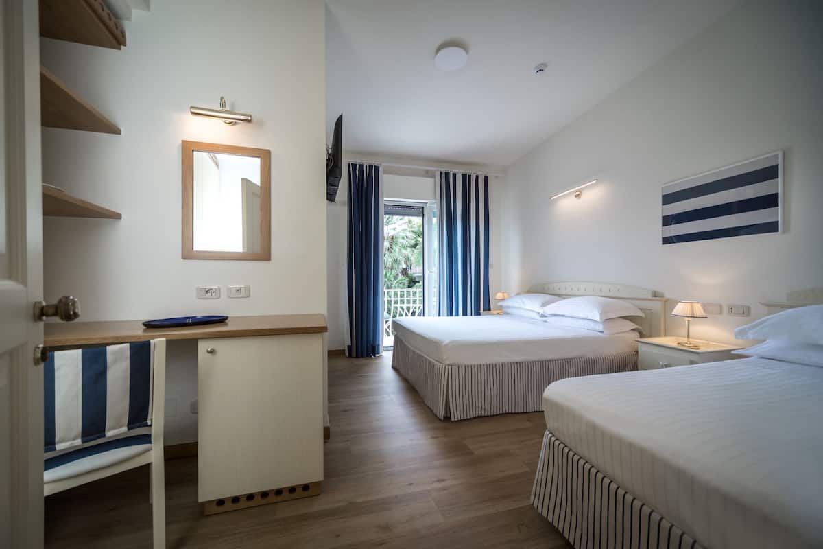 A hotel room with two beds, a desk, a mirror, and a view of the outdoors.