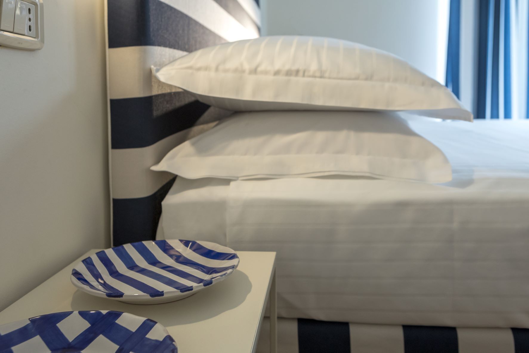 Quarto de hotel com cama, almofadas e toalha de mesa listrada.