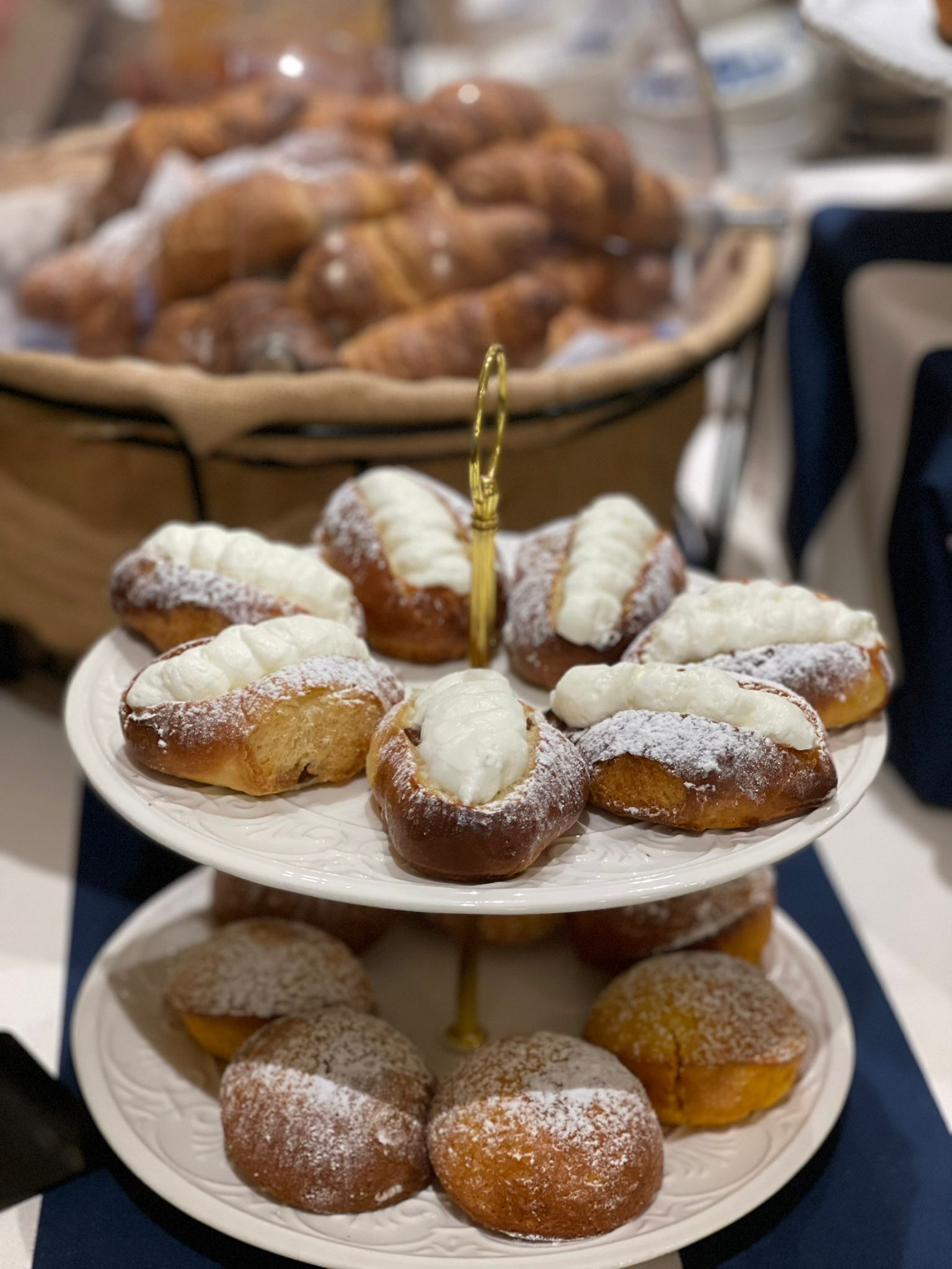 A three-tiered stand with pastries, including cream-filled pastries and powdered ones, on a white plate.