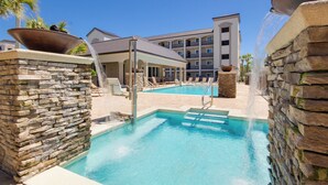 A pool area with stone walls, lounge chairs, and a building in the background. - Beach, Swim, Chill, Repeat – Alerio E202 (Miramar Beach)
