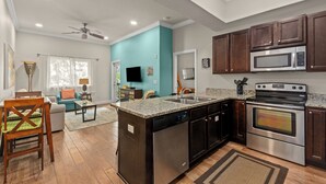 A modern kitchen with dark wooden cabinets, stainless steel appliances, and a teal accent wall. - Beach, Swim, Chill, Repeat – Alerio E202 (Miramar Beach)