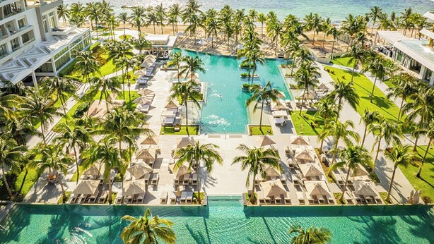 Un resort con piscina central, palmeras y vista al océano.