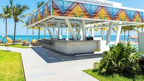 Un pabellón frente a la playa con techo de diseño geométrico, una zona de estar con sillas y vista al océano.