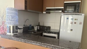 Eine Küche mit Granitarbeitsplatten, Holdekor-Schränken, einem Edelstahl-Wasserspender, einer Mikrowelle und einem Kühlschrank. Zwei hölzerne Barhocker stehen an der Theke.