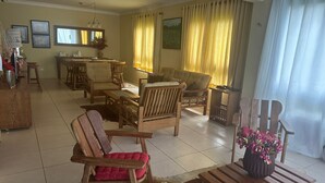 Ein geräumiges Wohnzimmer mit Essbereich, Holzmöbeln und einem großen Fenster mit Vorhängen.