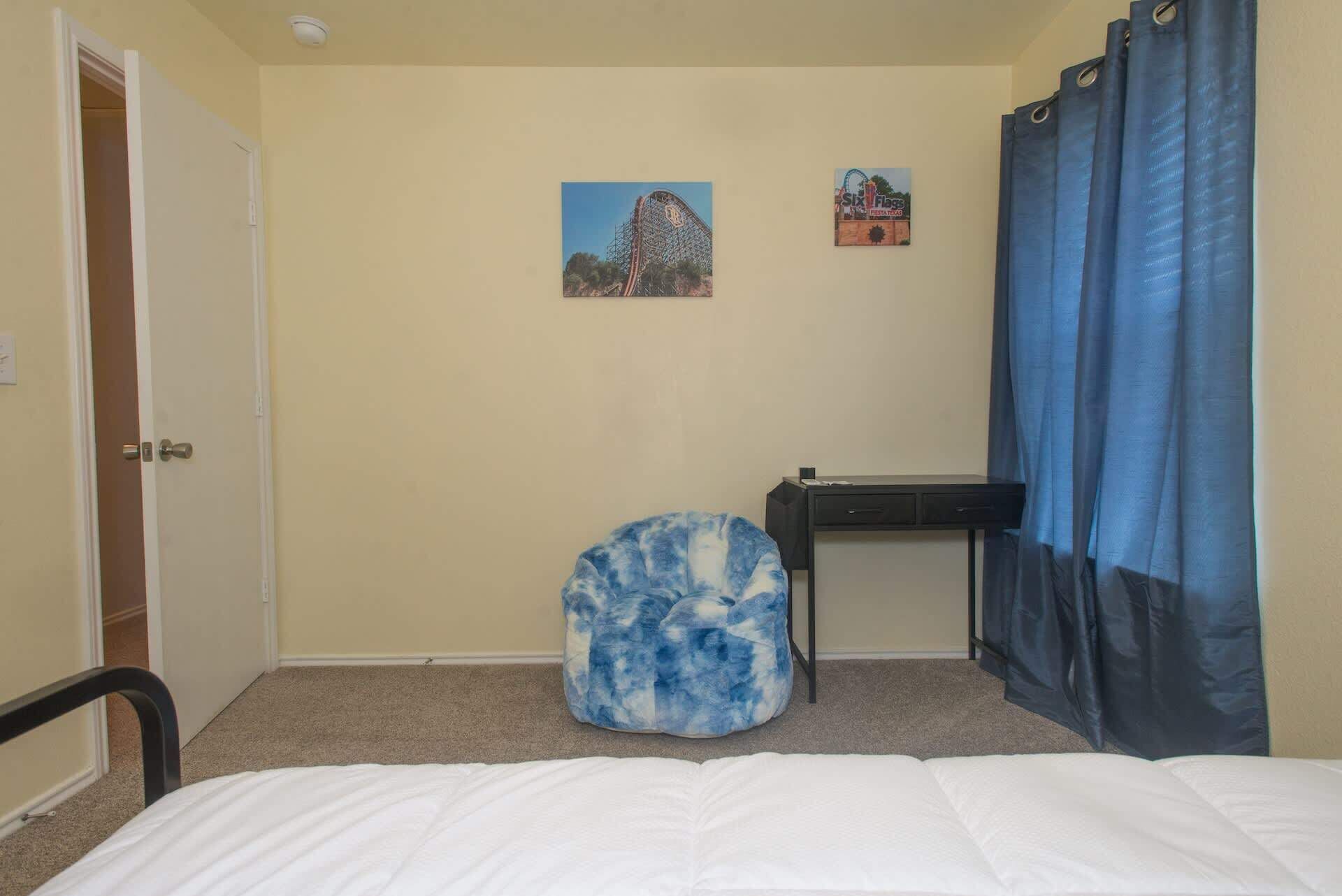 A bedroom with a bed, a desk, a chair, a blue curtain, and two wall decorations.
