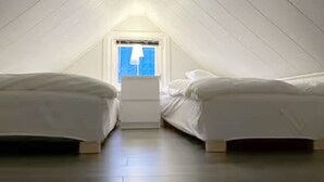 Ett litet, svagt upplyst sovrum på vinden med två sängar och ett fönster.