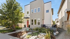 A modern two-story building with a red door, a small porch, and a landscaped front yard with rocks and plants. - Ram’s Roost | Rooftop Hot Tub, Patio & Family Fun (Fort Collins)