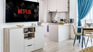A modern kitchen with a flat-screen TV displaying the Netflix logo, a dining area with a table and chairs, and a kitchen island with a sink and countertop. - ARI - AFI Mall Luxurious Apartments (Arad)