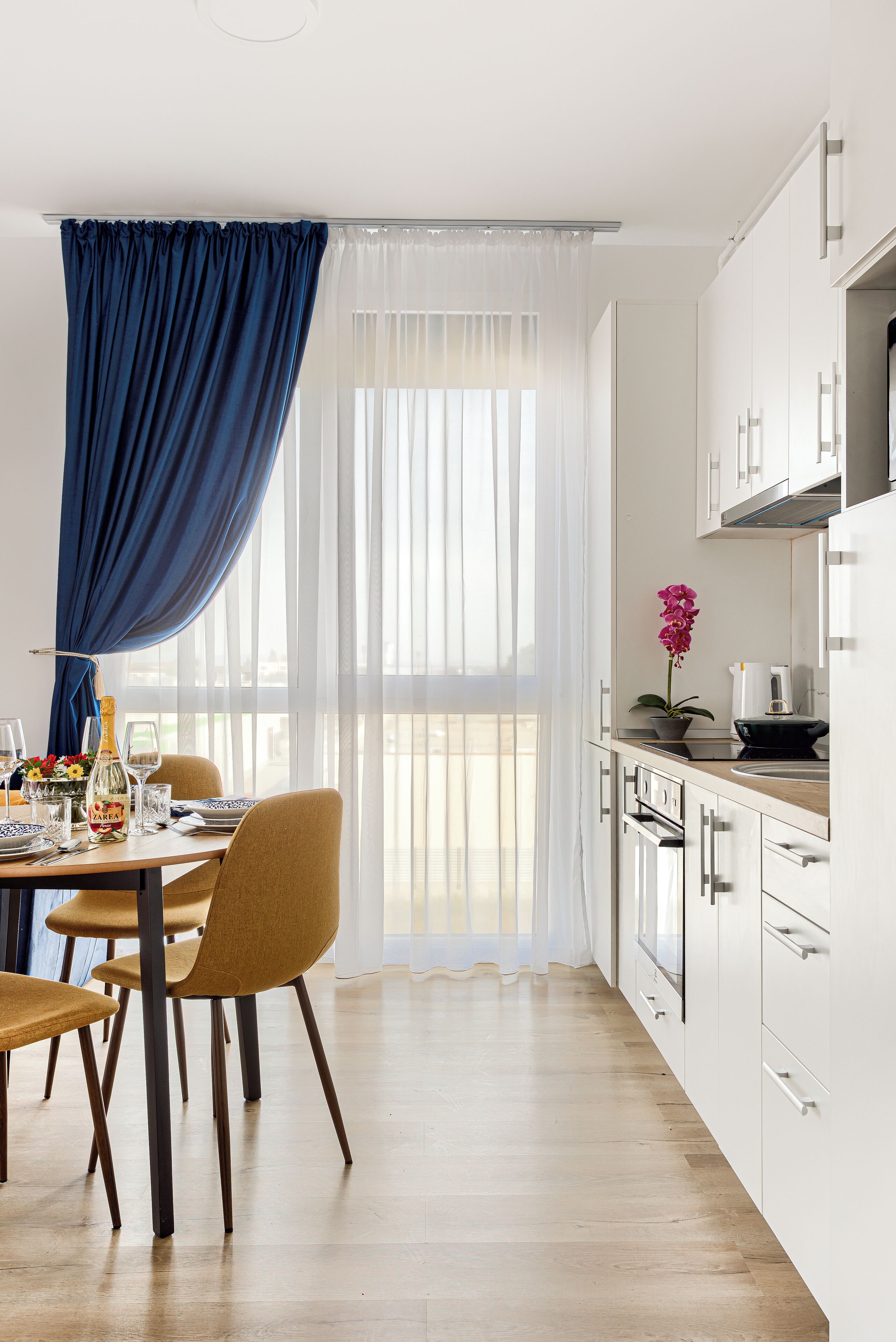 A modern kitchen with white cabinets, a wooden countertop, and a dining area with a table and chairs.