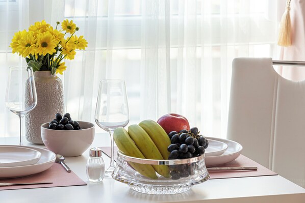 A dining table with a fruit bowl, wine glasses, and a vase with yellow flowers.