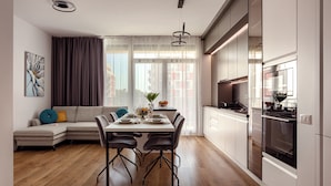 A modern kitchen with a dining area, wooden flooring, and a large window with curtains. - ARI - AFI Mall Luxurious Apartments (Arad)