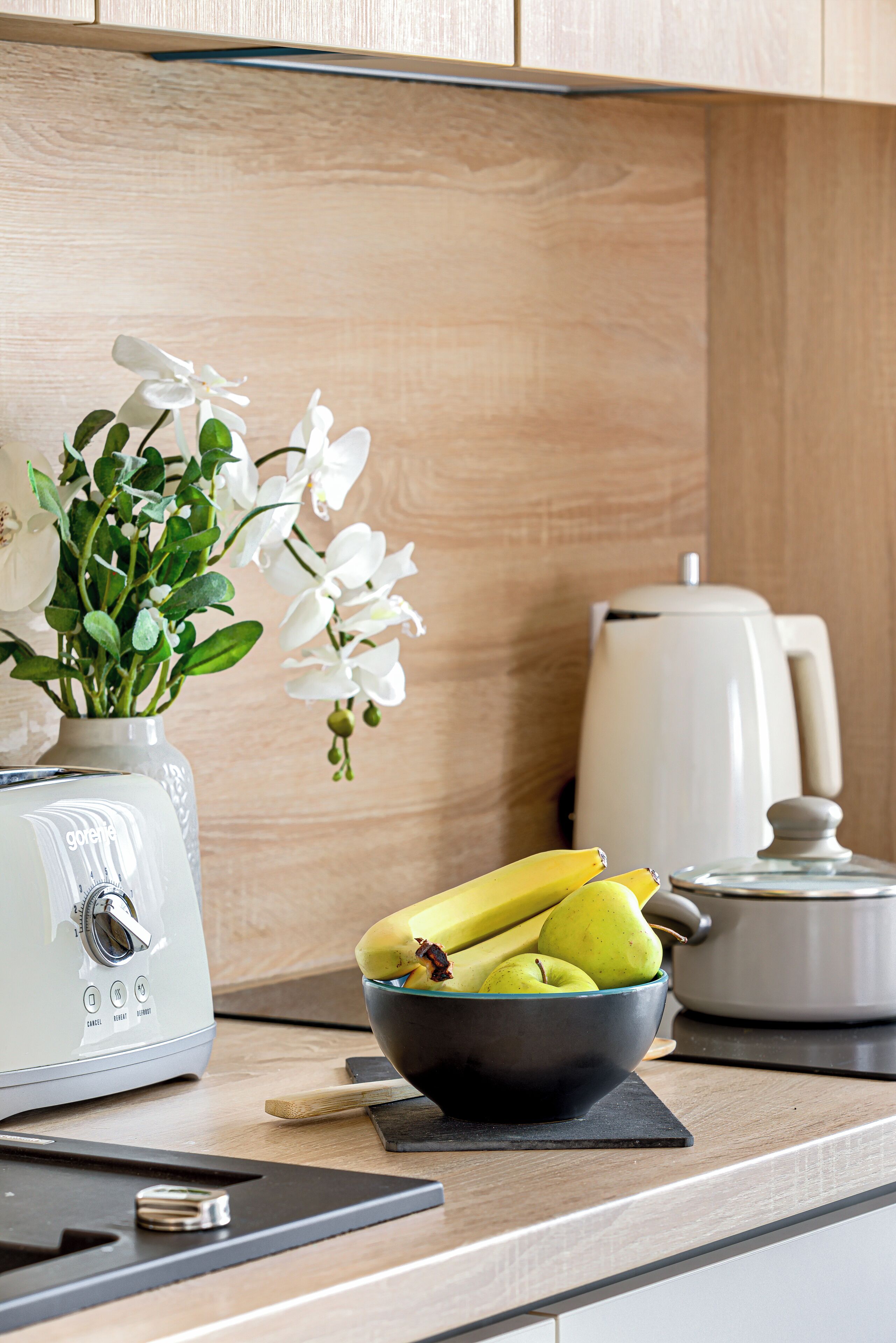 A kitchen with a white toaster, a bowl of fruit, and a white coffee maker on the counter.