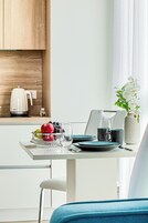A modern kitchen with a white countertop, a kettle, a bowl of fruit, and a vase with flowers.