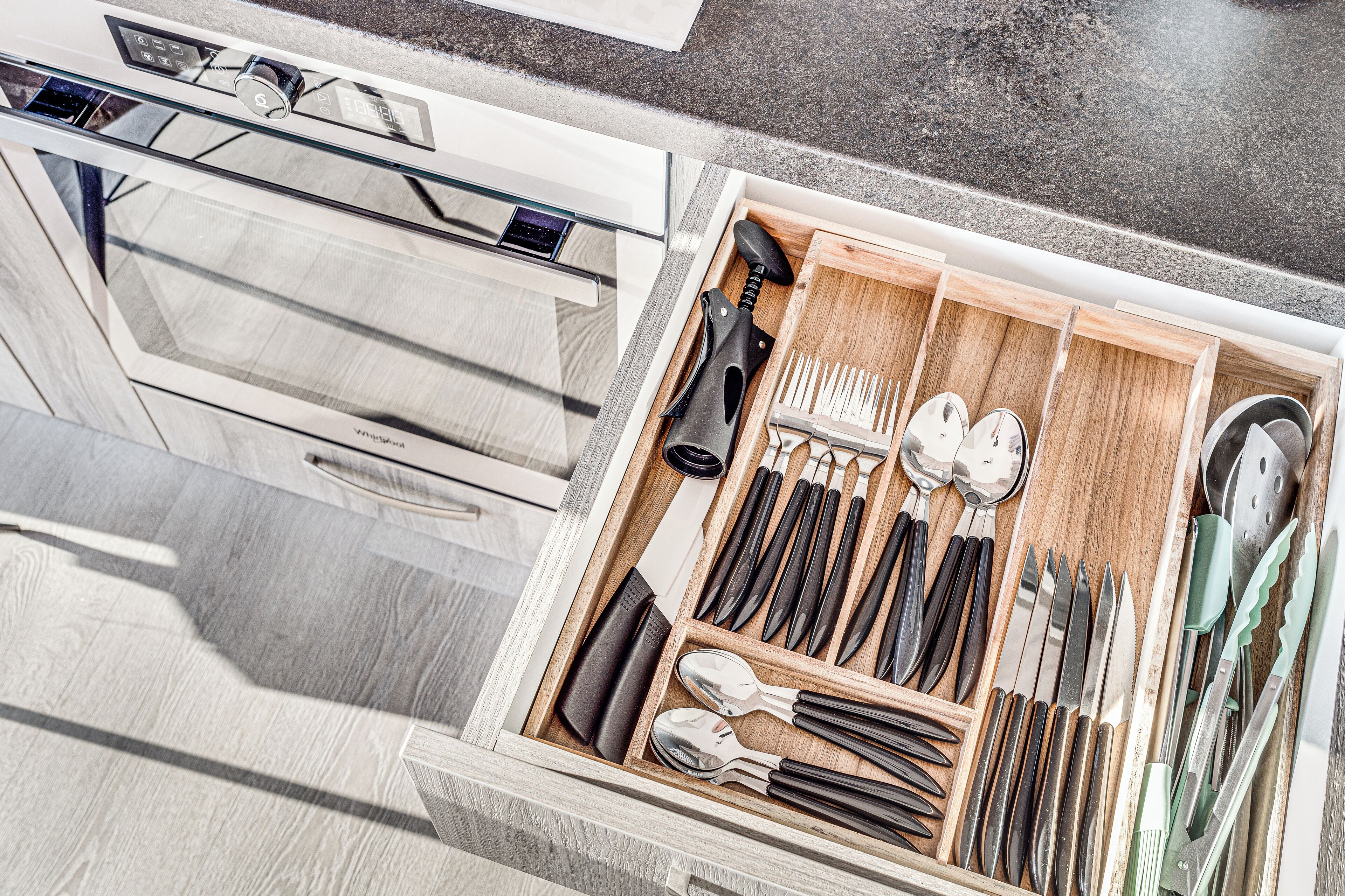 A drawer with neatly organized kitchen utensils including knives, spoons, and a cutting board.