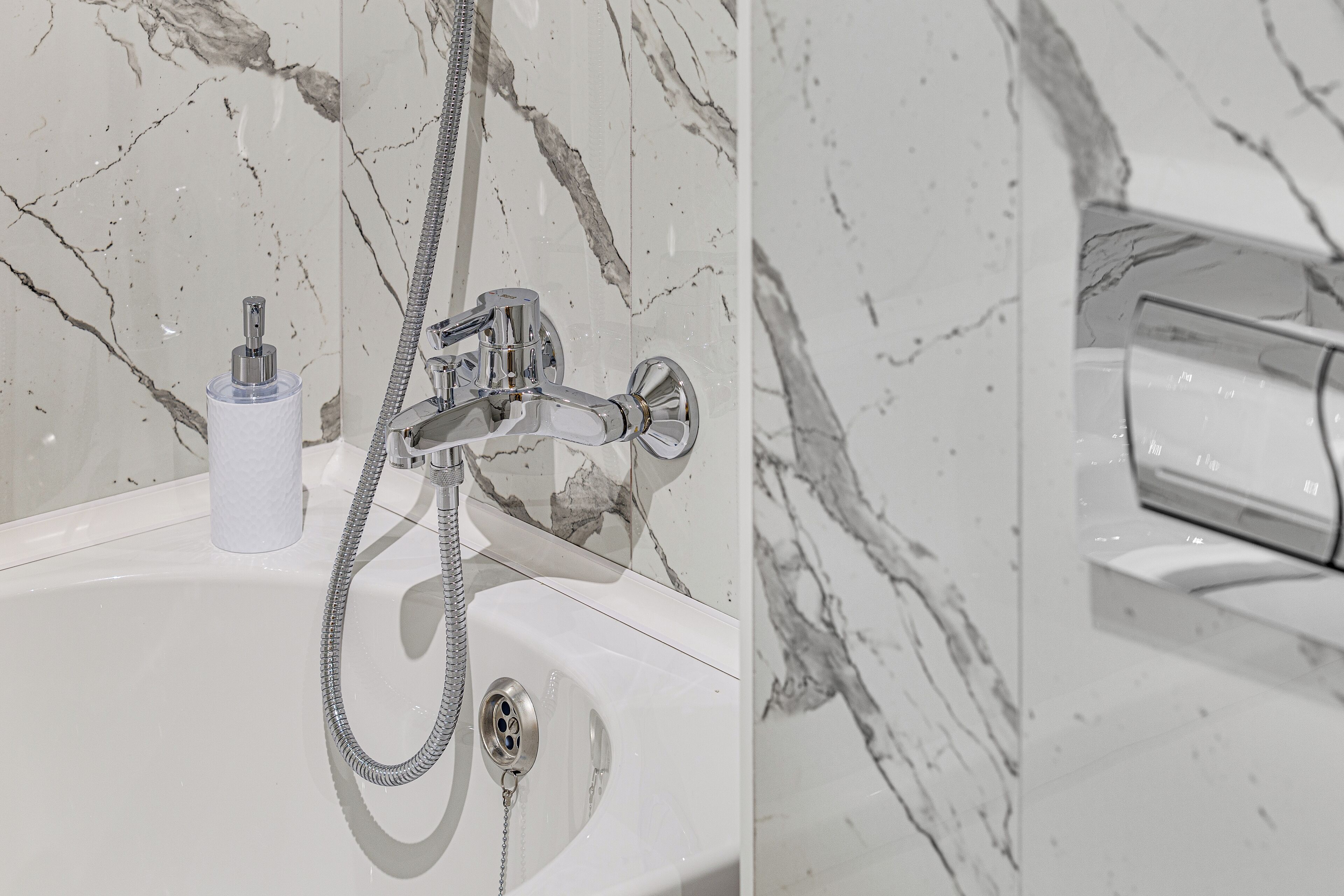 Un bagno con parete in marmo, lavabo bianco e doccia con soffione a mano.