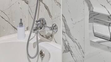 Un bagno con parete in marmo, lavabo bianco e doccia con soffione a mano.