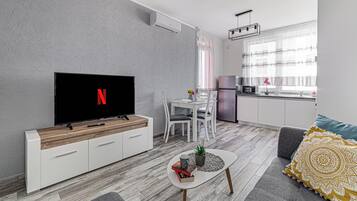 En moderne stue med et fladskærms-tv, et spiseområde med bord og stole, og et køkken med køleskab og vask.