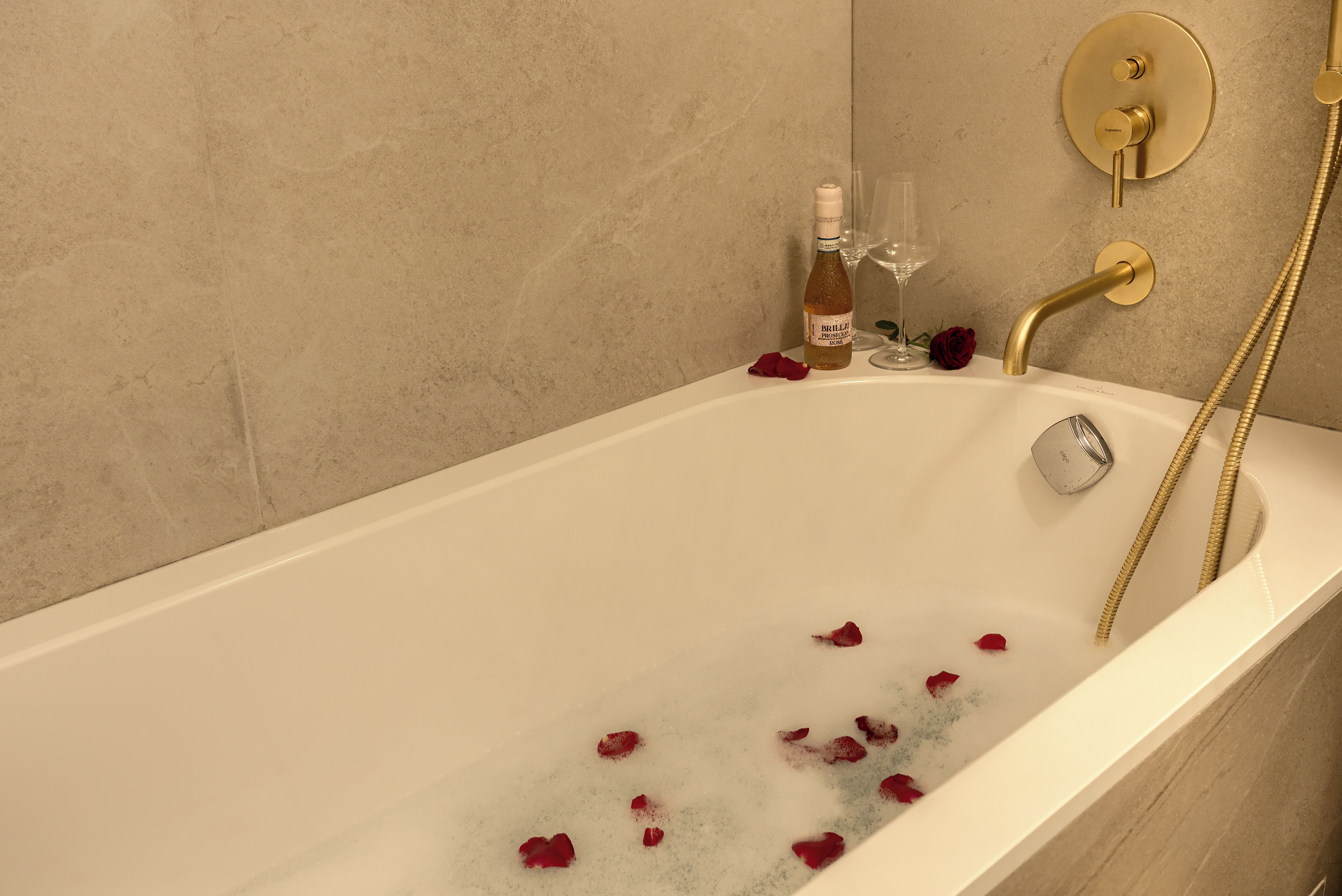 Una bañera con pétalos de rosa, una botella de Brilla y una copa.