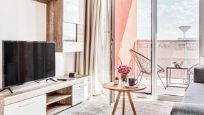 A modern living room with a flat-screen TV, wooden furniture, a round table with a vase of flowers, and a sliding glass door leading to a balcony. - ARI - AFI Mall Luxurious Apartments (Arad)