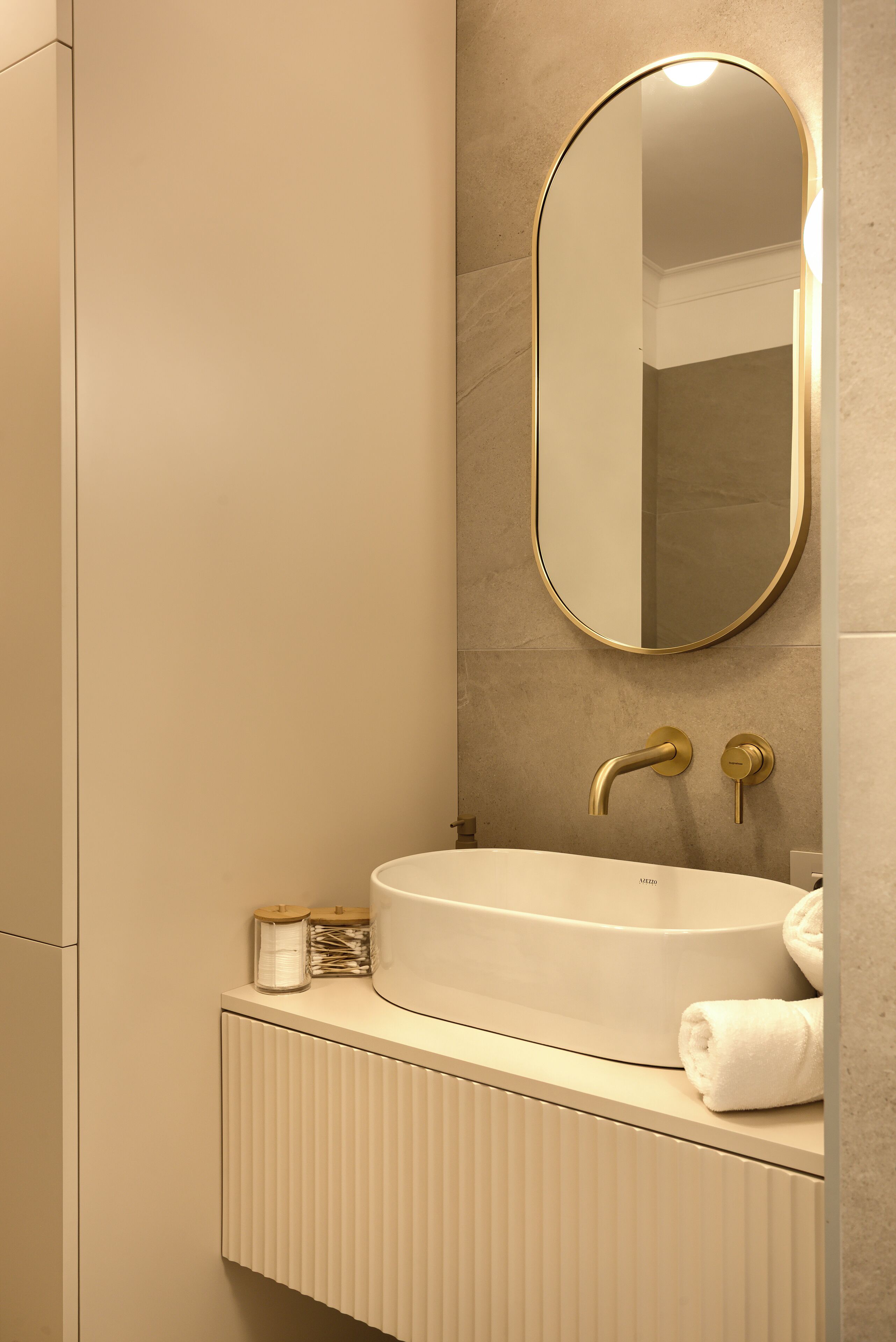 Un baño moderno con un lavamanos blanco, detalles dorados y un espejo grande.