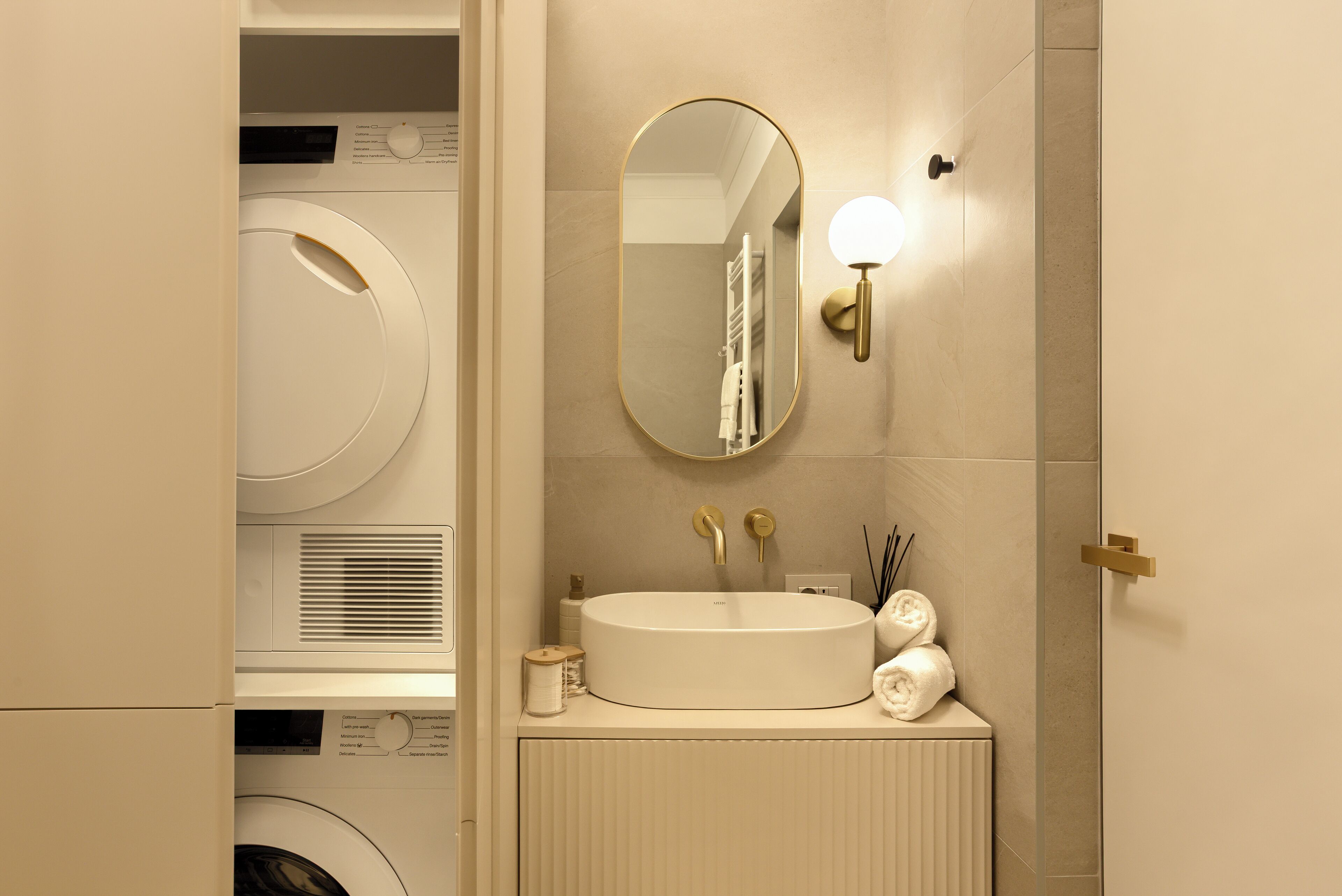 A modern bathroom with a built-in washing machine, a large oval sink, and a wall-mounted mirror.