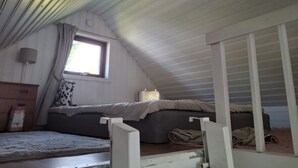 A bedroom with a sloped ceiling, a window with curtains, a bed with a blanket, and a bedside table with a lamp. - Beachfront holiday home with sea view in Sölvesborg | SE03021 (Sölvesborg)