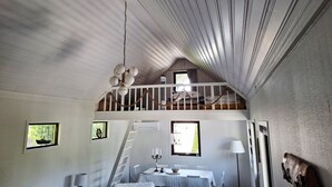 A loft-style bedroom with a sloped ceiling, a chandelier, a loft bed, a dining table with chairs, and a ladder leading to the loft. - Beachfront holiday home with sea view in Sölvesborg | SE03021 (Sölvesborg)