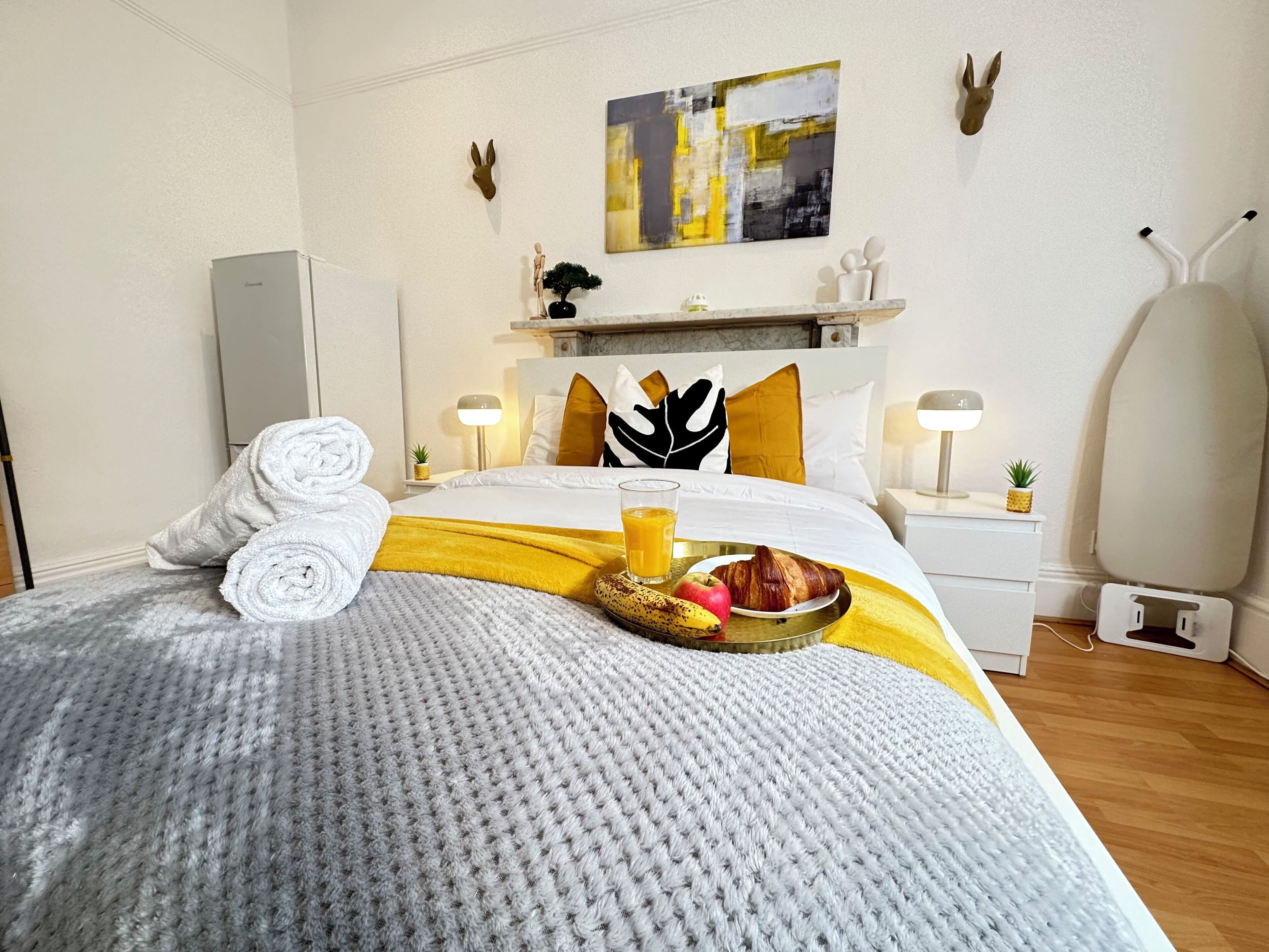 A neatly made bed with a yellow and white blanket, a tray with breakfast items, and a painting on the wall.