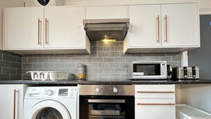 A compact kitchen with white cabinets, a washing machine, an oven, a microwave, and a toaster.