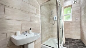 A bathroom with a white sink, a glass shower enclosure, and beige tiled walls.