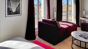 A hotel room with a bed, a desk, a chair, a window with curtains, and a framed picture on the wall. - Eiffel Yard Hotel (Paris)