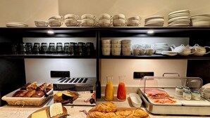 A buffet with various food items, including bread, cheese, and meats, and a selection of cups and plates on shelves. - Eiffel Yard Hotel (Paris)
