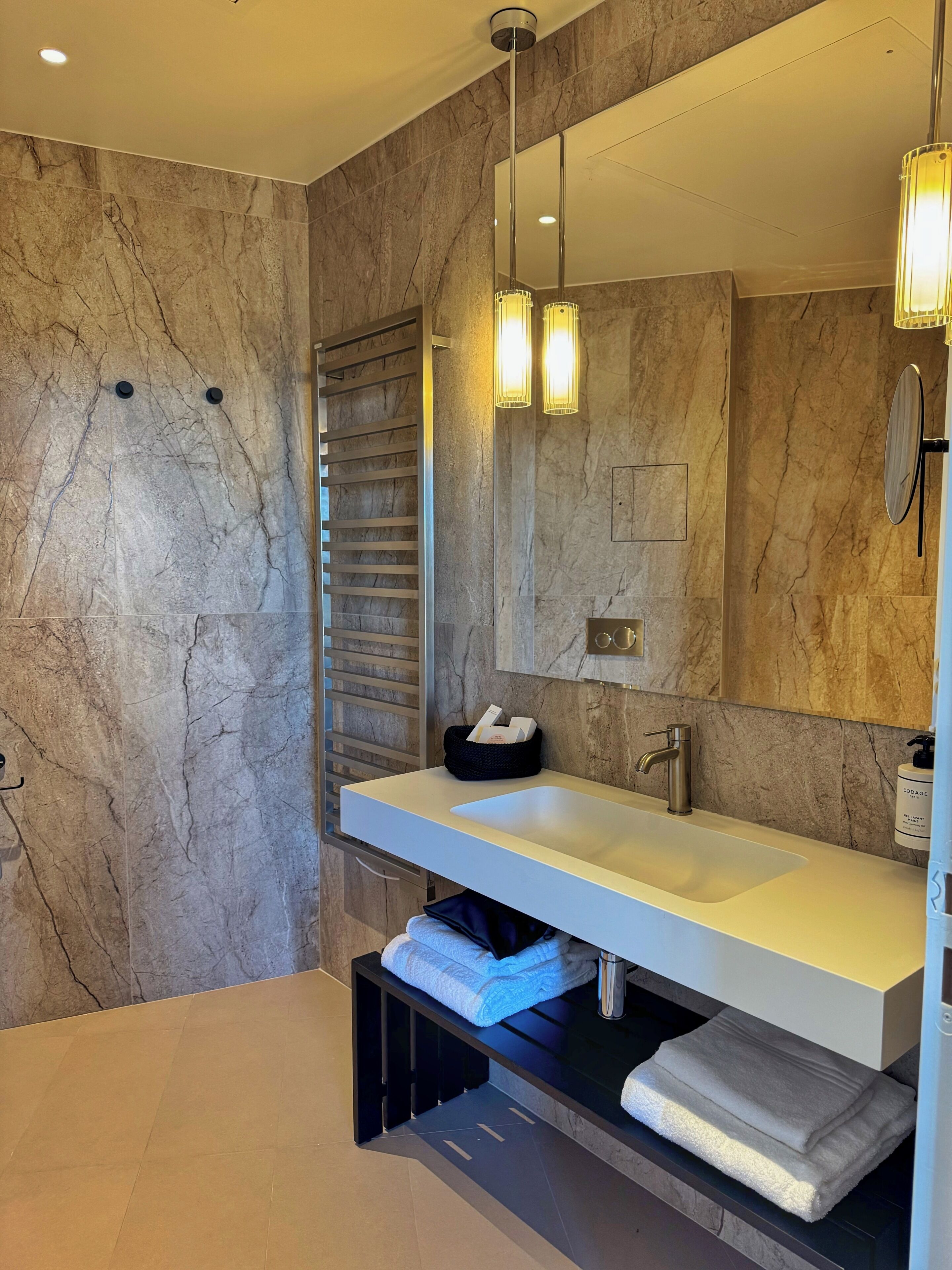 A modern bathroom with a marble wall, a large mirror, a white sink, and a towel rack.