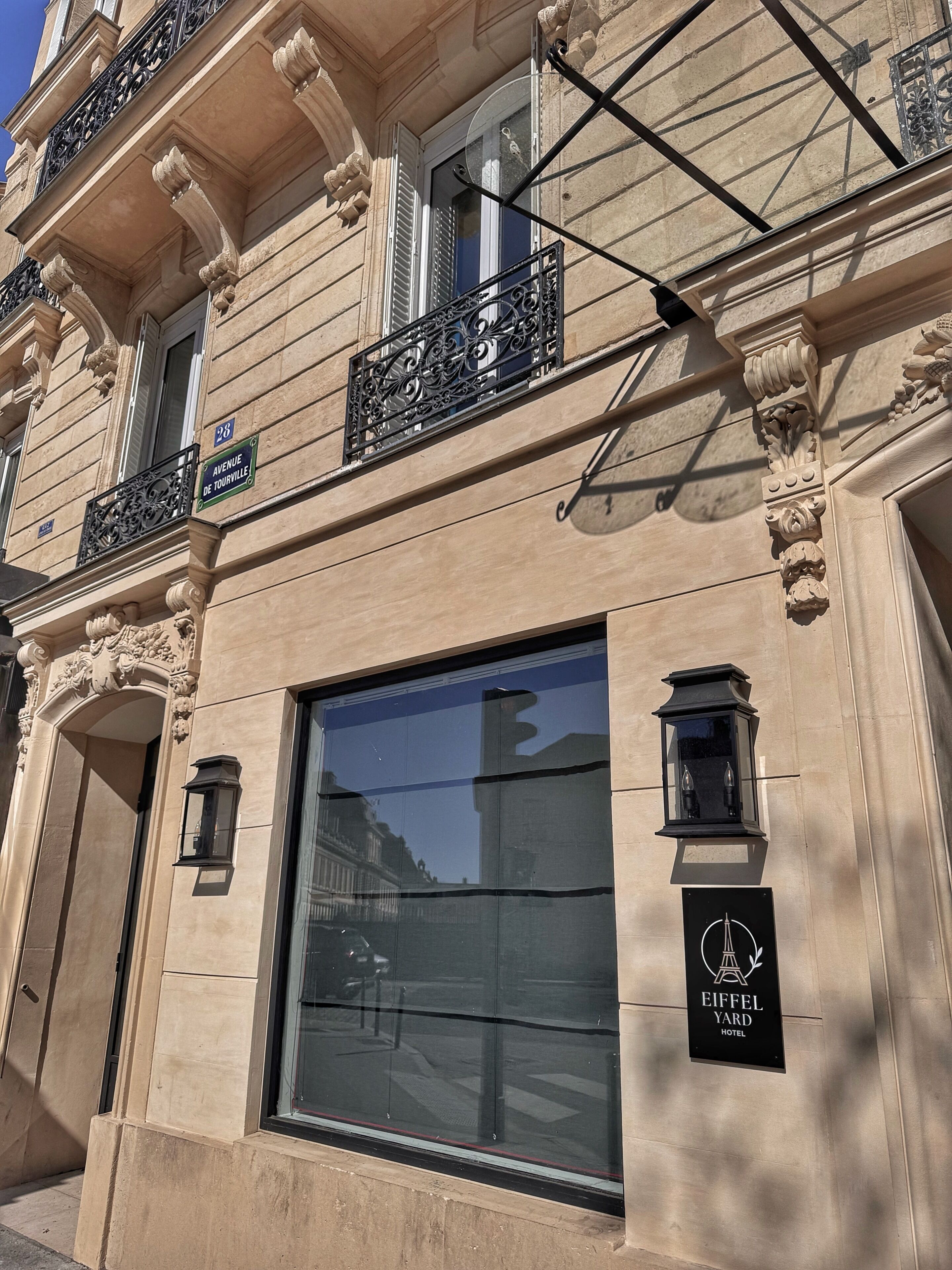 A building facade with a large window, a street sign reading 'Avenue de Tourville,' and a sign for 'Eiffel Yard Hotel.'