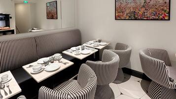 Un comedor moderno con asientos a rayas, una mesa larga dispuesta para cuatro comensales y un cuadro abstracto de gran tamaño en la pared.