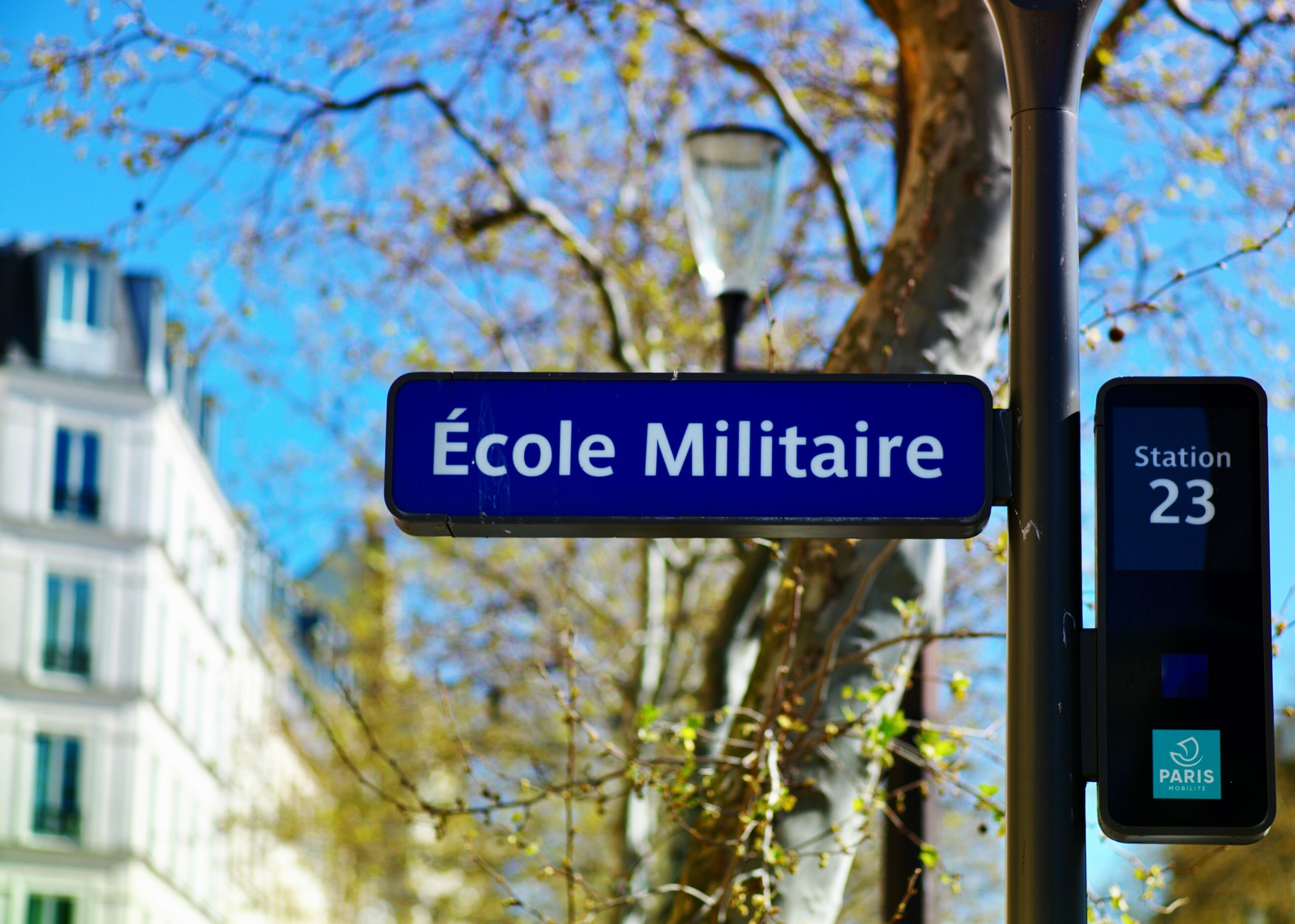 A street sign for 'École Militaire' and a digital display for 'Station 23' with the Paris Mobilite logo.