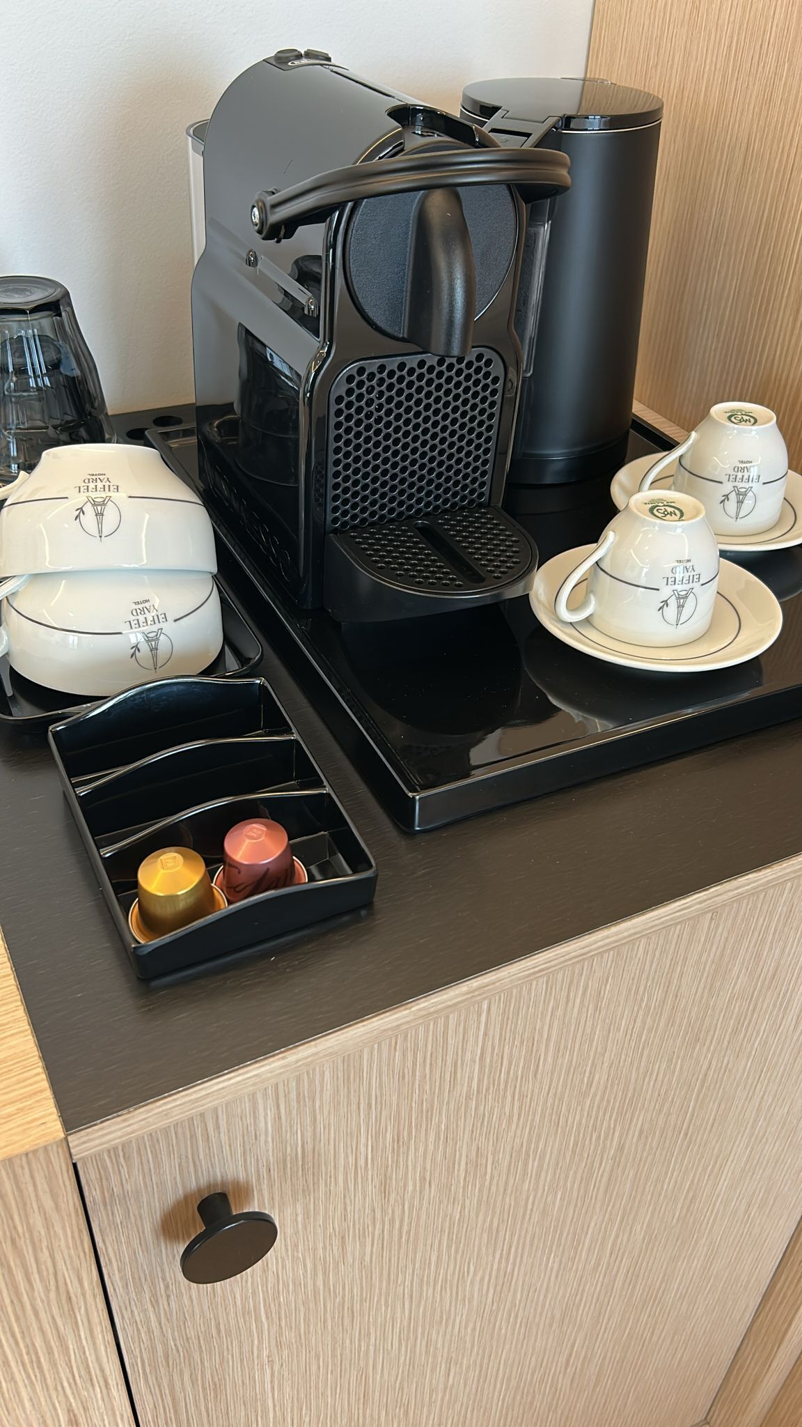 A coffee maker, a coffee pot, a tray with cups and saucers, and a drawer with containers.