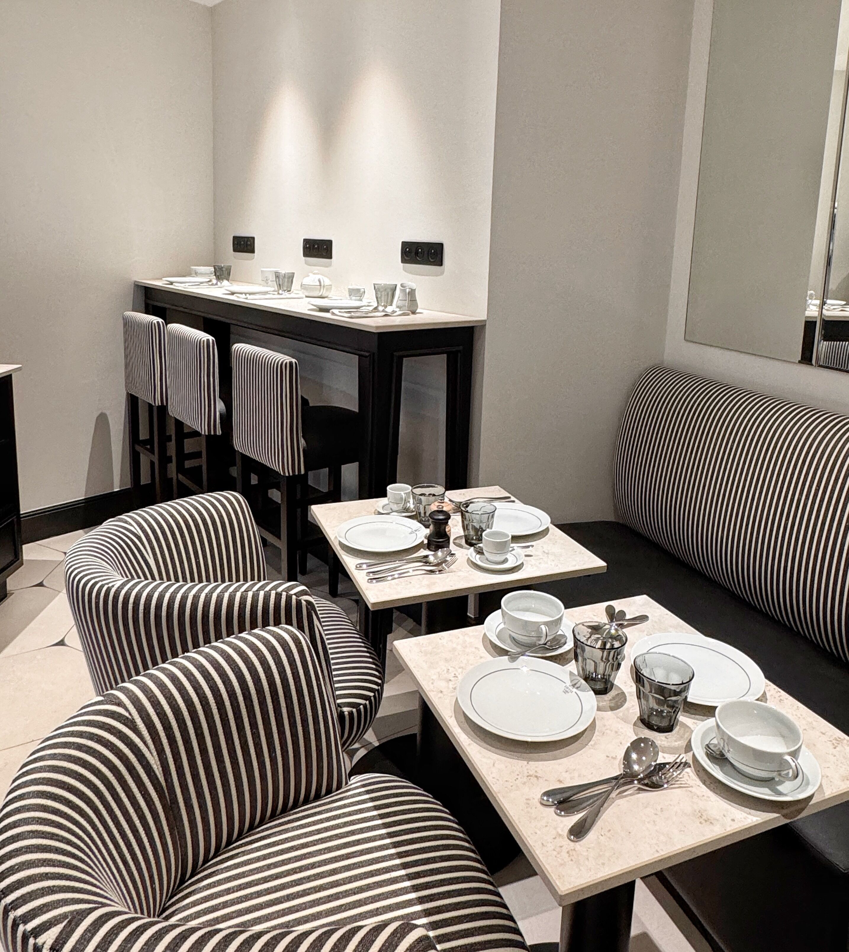 A dining area with striped chairs and tables, equipped with plates, cups, and cutlery.