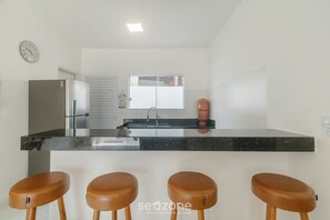 A modern kitchen with a central island, stainless steel refrigerator, and a clock on the wall. - 4-bedroom Apart in Condominium With Pool Vif0104 (Porto Seguro)