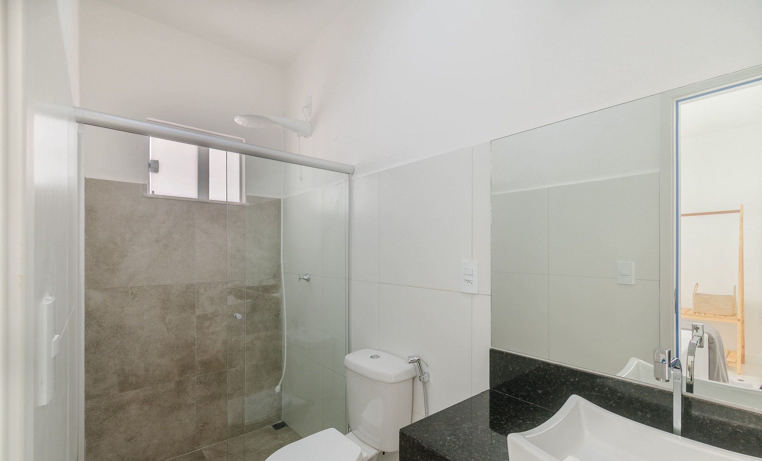 A modern bathroom with a glass shower enclosure, a white toilet, and a black countertop with a sink.