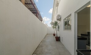 A narrow concrete pathway between buildings, with potted plants and a window on the right. - 4-bedroom Apart in Condominium With Pool Vif0104 (Porto Seguro)
