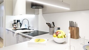 Een moderne keuken met een inbouwfornuis, een koffiezetapparaat, een schaal met fruit en een messenblok.