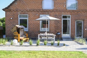 Une maison en briques avec un patio, du mobilier d’extérieur et un grand parasol.