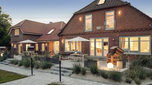 Een woonhuis van baksteen met twee verdiepingen, een terras, buitenmeubilair en een goed verlichte ingang.